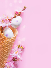 Creative Easter vertical photo with bokeh und copy space. Easter eggs and pink flowers in a waffle cone for ice cream. Happy and joyful Easter. Church Christian holidays, Christianity