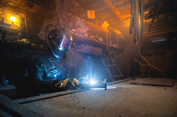 welder in a workshop welds a metal part. General plan of an old cluttered garage where a man in...