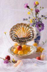 delicate still life with yellow and red cherry plum berries in a special crystal vase in the shape of a shell