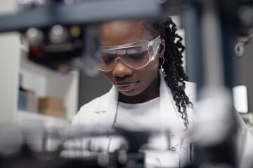Close up shot of African American female technician in safety glasses looking down while working in...