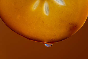 Slice of persimmon with juice drops on a orange background, macro photography. Texture fresh fruit, closeup