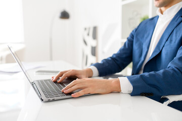 Cropped photo of hands of male office employee mid-typing on a laptop, sitting in office space. The image illustrates the day-to-day engagement and concentration that business tasks require.