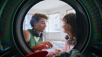 Couple talking public laundromat closeup. Smiling friends wait in laundry room