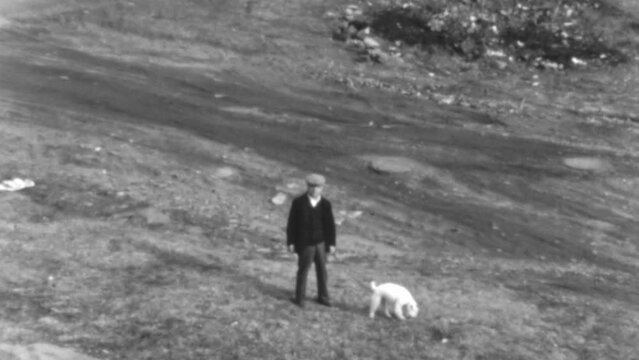 Man Enjoys a Peaceful Walk with His Dog Across a Gently Sloping Grassy Landscape During the Evening Hours. Luxury Life in New York City 1930s. Black and White Vintage Footage of Great Depression Era