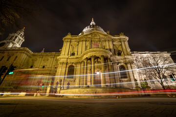 A street view of the facade of St. Paul's Cathedral at night time with light trails from passing vehicles.