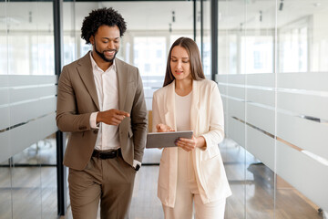 An African-American businessman points at a tablet, discussing the content with his female...