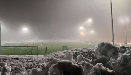 Lots of snow and green soccer field in the fog