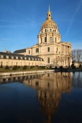 Fototapeta na wymiar Dôme des Invalides, célèbre monument à Paris, se reflétant dans l’eau gelée d’une fontaine dans un jardin (France)