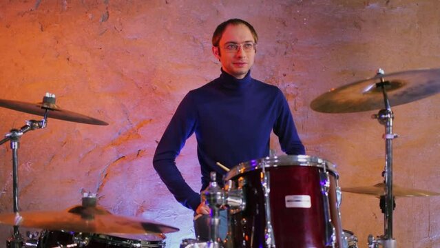 Drummer hits cymbals by drumstick near illuminated wall
