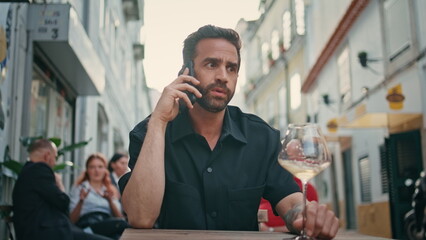 Nervous man talking smartphone at urban bar close up. Businessman holding wine