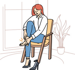 Woman with varicose veins feels pain in legs due to uncomfortable high-heeled shoes, sits on chair in apartment. Girl needs medicinal ointment to cure varicose veins or calluses on heel