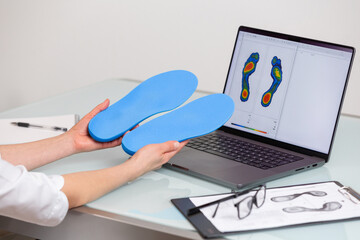 Female doctor orthopedist  holding custom made insoles in a clinic in front of the laptop with a test feet picture.  Feet recreation and orthotic medicine concept - 718339977