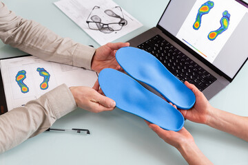 Female doctor orthopedist  presents new custom made insoles to a male patient in a clinic. - obrazy, fototapety, plakaty