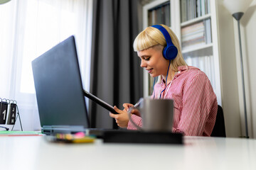Young blonde woman smiling while working on her laptop and drinking coffee