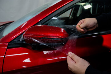 Naklejka premium The master applies vinyl film to the side view mirror of a car. 