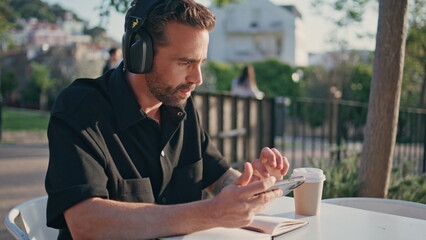 Latin freelancer texting mobile phone at park table closeup. Man listening music