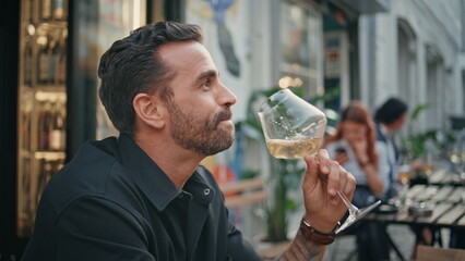 Bearded guy tasting wineglass open air restaurant closeup. Man enjoying alcohol