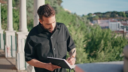 Pensive author writing notebook cityscape place alone close up. Man making notes