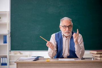 Old male teacher in front of green board