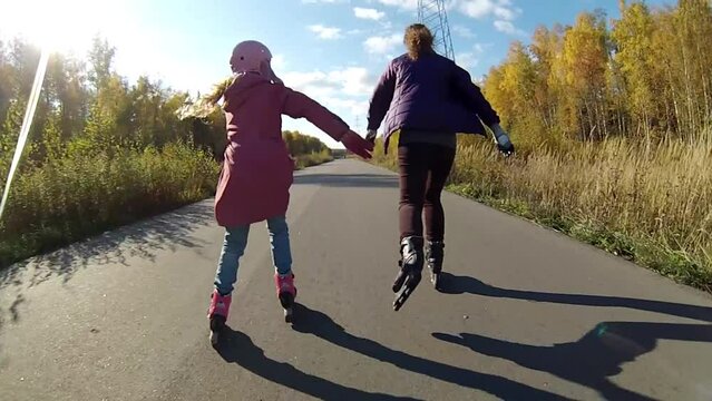 Back of woman and girl roller skating on road at fall sunny day