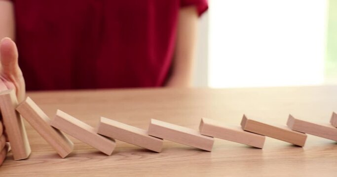 Closeup of businesswoman hand stopping domino effect with hand at table