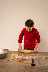 Niño chef amasando y haciendo galletas para San Valentín aplanando la masa con rodillo y...