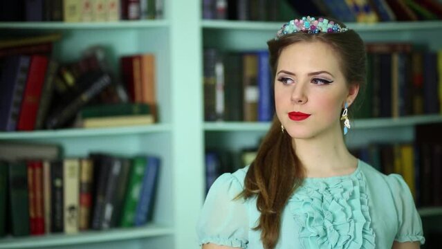 woman in cyan dress and jewelery on head stand near book shelves