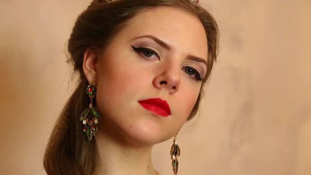 Young woman turns head and looks forward with earrings near wall