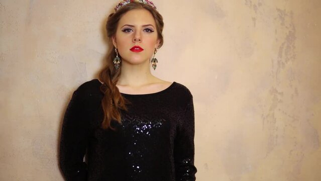 Girl in black blouse and jewelery stands near wall at studio
