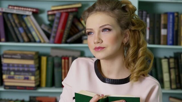 Young woman holds book near book shelves in library