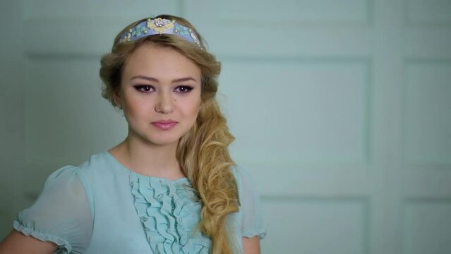 Young blonde smiles in blue dress and diadem on head