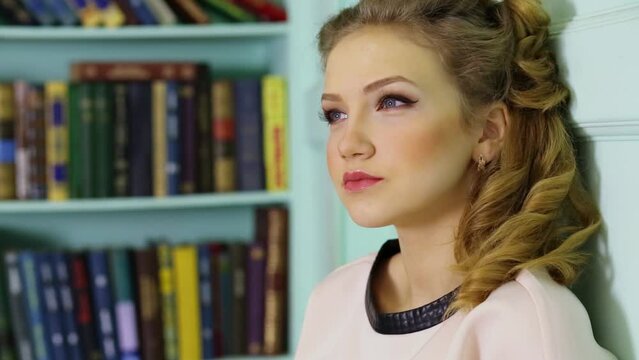 Attractive young woman looks aside near book shelves in library