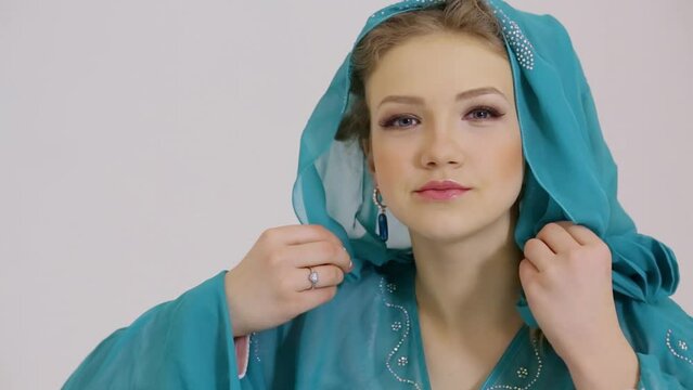 Handsome young woman adjusts cyan dress with hood on head in studio