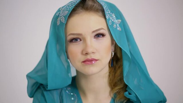 Attractive woman smiles in cyan dress with hood on head at studio