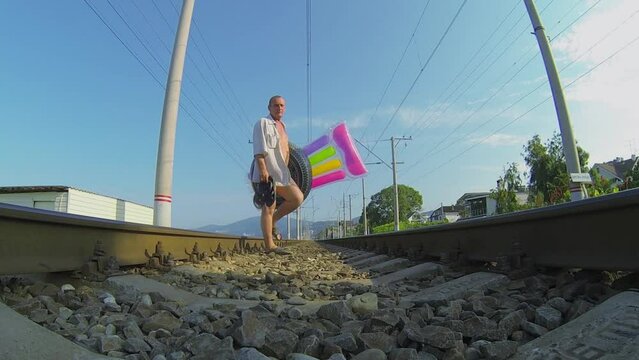 Retiree man with beach stuff walks by railway at summer