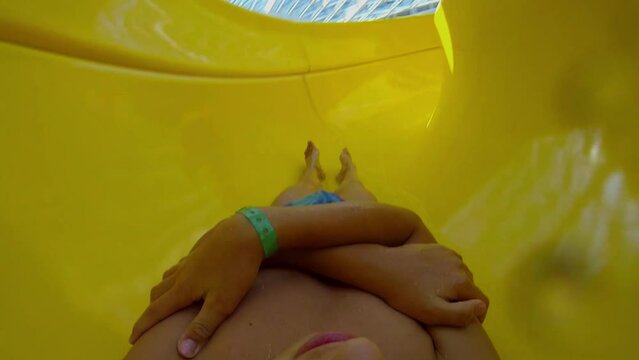 Young boy slides by yellow tube to water in aquapark. 