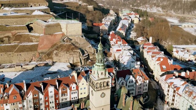 Historical clock tower of Klodzko town hall with fortress in the background. Old town city hall close up. Winter cityscape panorama, aerial view.