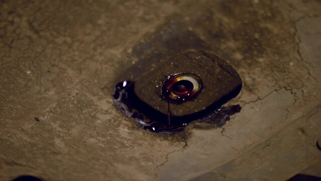 Close-up video of car oil draining from the crankcase during replacement. Filming the work of a car mechanic with front lighting.