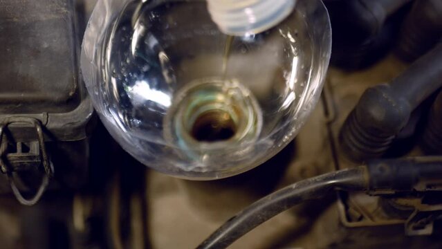 The process of pouring engine oil into a car crankcase at a car service center. Close-up shot, front suspension.