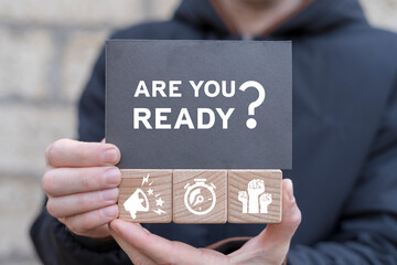 Business and Are you ready? concept. Man holding wooden cubes with icons and black sticky note with text: ARE YOU READY?