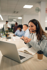 Smiling caucasian woman working in a call center and using a laptop and headset