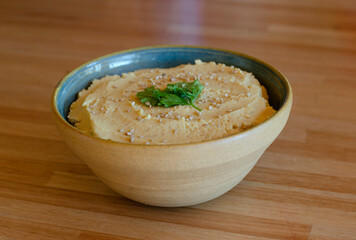 chickpea hummus with sesame seeds and parsley on wooden table in natural light