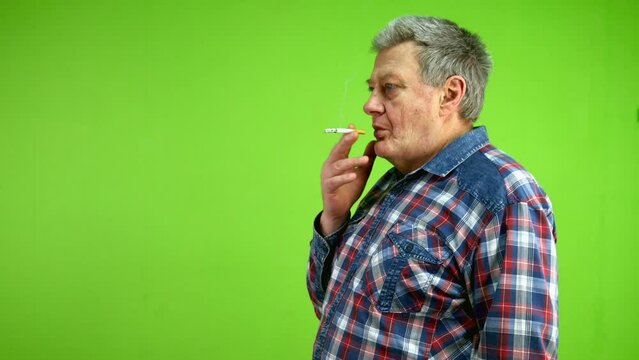 Senior man smoking cigarette and blowing smoke.