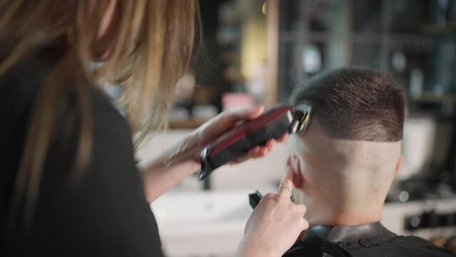 Young female barber making men's undercut haircut hairstyle using Haircut Clipper in Modern style barber shop. Haircare service local small business, cosmetics and personal care industry 4K video