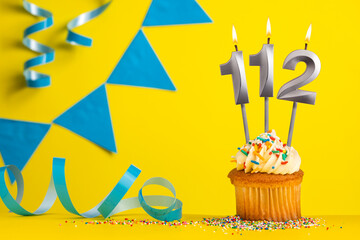 Lighted birthday candle number 112 - Yellow background with blue pennants