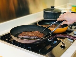 Partial close-up view of woman holding frying pan with grilled steak and rosemary