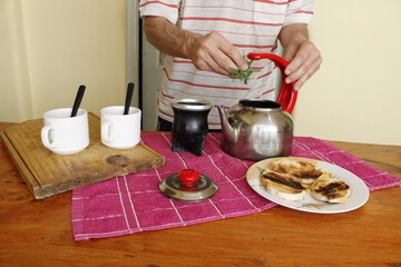 El hombre prepara el té argentino sudamericano, colocando las hierbas verdes en la tetera, para...