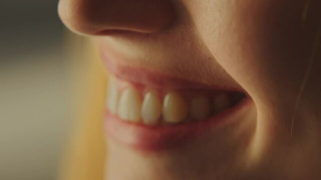Extreme close-up view of a young caucasian woman smiling. Camera focus on woman's white teeth and brown eyes