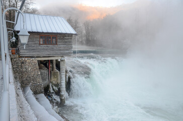 Water mill surrounded by ice, fog and snow. River in winter day. Mountain river flowing. 