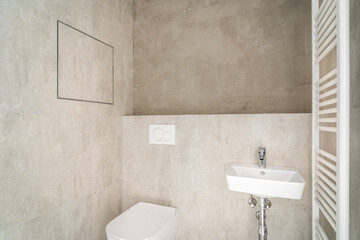 Small bathroom with modern beige tiling,wc and sink. Room is in process of construction or reconstruction,because part of wall is not covered with tiles,and therefore toilet is not yet completed.